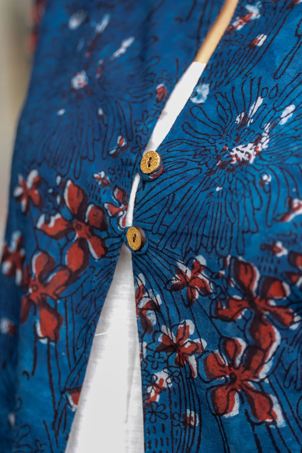 Close-up of a blue patterned garment with red and white floral print, featuring two gold-toned buttons and a white inner lining.